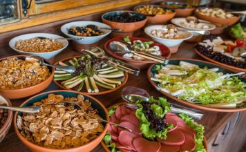 Açık büfe anlayışı aslında yüzyıllar öncesine dayanan bir paylaşım kültürünün modern yansımasıdır. İnsanlar topluluk halinde yemek yerken, farklı seçenekler sunma geleneği tarih boyunca birçok toplumda görülmüştür. Özellikle Osmanlı’da ziyafet sofraları, Avrupa’da ise şölenler bu anlayışın temellerini oluşturmuştur. Günümüzde ise otellerden restoranlara, davetlerden kutlamalara kadar pek çok alanda açık büfe yaygın olarak tercih edilmektedir. Konulu bir haber görseli.