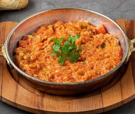 Türk mutfağının en sevilen kahvaltı yemeklerinden biri olan menemen, yıllardır süren büyük bir tartışmanın da merkezinde yer alıyor. Asırlardır sofralarda yer bulan bu lezzet, basit malzemelerle hazırlanmasına rağmen, “Soğansız mı olur yoksa soğanlı mı olmalı?” sorusu etrafında hararetli tartışmalara neden oluyor. Konulu bir haber görseli.