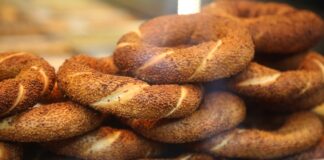 Simit, Osmanlı döneminden günümüze kadar gelen köklü bir geçmişe sahiptir. İlk olarak saray mutfaklarında farklı un karışımlarıyla yapılan bu lezzet, zamanla halk arasında yaygınlaşarak günlük yaşamın bir parçası haline gelmiştir. Özellikle 16. yüzyıldan itibaren İstanbul’da simit fırınlarının açılmasıyla birlikte, bu eşsiz yiyecek şehir kültürünün önemli bir unsuru olmuştur. Bugün Anadolu’nun dört bir yanında farklı isimlerle anılsa da, ortak nokta simidin sofralarda her daim yer bulmasıdır. Konulu bir haber görseli.