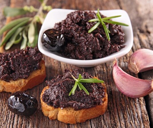 Tapenade, özellikle Fransız ve Akdeniz mutfağının vazgeçilmez zeytin ezmesi olarak biliniyor. Temel malzemeleri arasında siyah zeytin, kapari, zeytinyağı ve bazen ançüez bulunuyor. Bu malzemeler mutfak robotunda püre haline getirilerek homojen bir kıvam elde ediliyor. Hazırlanışı oldukça basit olsa da, malzemelerin kalitesi ve tazeliği ezmenin lezzetini doğrudan etkiliyor. Konulu bir haber görseli.
