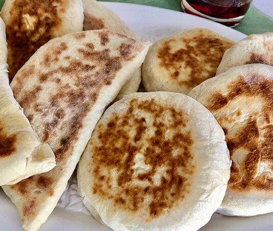 Türk mutfağının en özel ve sevilen ekmek çeşitlerinden biri olan bazlama, yumuşak dokusu, doyurucu yapısı ve mis gibi kokusuyla sofraların vazgeçilmezidir. Özellikle Anadolu’nun birçok bölgesinde kahvaltıların, çay saatlerinin ve hatta ana yemeklerin yanında sıklıkla tercih edilen bu ekmek, sadece lezzetiyle değil kültürel bir değer olarak da öne çıkar. Günümüzde modern sofralarda da kendine yer bulan bazlama, hem geleneksel hem de pratik bir lezzet olarak dikkat çekmektedir. Konulu bir haber görseli.