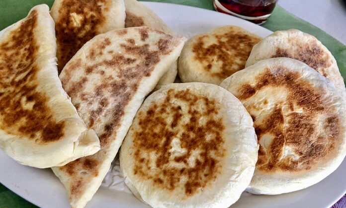 Türk mutfağının en özel ve sevilen ekmek çeşitlerinden biri olan bazlama, yumuşak dokusu, doyurucu yapısı ve mis gibi kokusuyla sofraların vazgeçilmezidir. Özellikle Anadolu’nun birçok bölgesinde kahvaltıların, çay saatlerinin ve hatta ana yemeklerin yanında sıklıkla tercih edilen bu ekmek, sadece lezzetiyle değil kültürel bir değer olarak da öne çıkar. Günümüzde modern sofralarda da kendine yer bulan bazlama, hem geleneksel hem de pratik bir lezzet olarak dikkat çekmektedir. Konulu bir haber görseli.