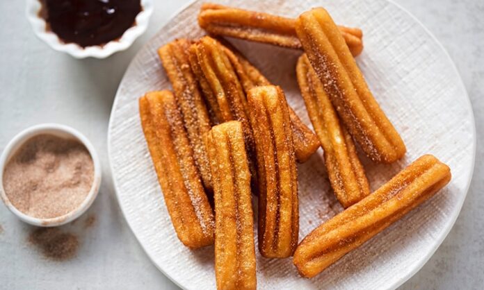 Churros, İspanya kökenli, kızartılarak hazırlanan tatlı hamur çubuklarıdır. 19. yüzyılda İspanya’da ortaya çıkan bu lezzet, kısa sürede Latin Amerika ve dünyanın farklı bölgelerine yayılmıştır. Geleneksel olarak kahvaltıda veya akşamüstü çay saatlerinde tüketilen churros, sıcak çikolata veya karamel sosla birlikte sunulur. Konulu bir haber görseli.