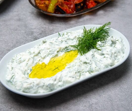 Haydari İle Sofralara Ferahlık Katın Haydari, özellikle kahvaltı sofralarının ve mezelerin vazgeçilmez tatlarından biridir. Yoğurt bazlı bu lezzetli meze, hem hafif hem de besleyici olmasıyla öne çıkar. Haydari, yüksek protein içeriği sayesinde kas ve kemik sağlığını desteklerken, probiyotik özelliği ile sindirim sistemine katkıda bulunur. İçerdiği sarımsak ve dereotu gibi doğal malzemeler, lezzetin yanı sıra sağlık açısından da avantaj sağlar. Konulu bir haber görseli.