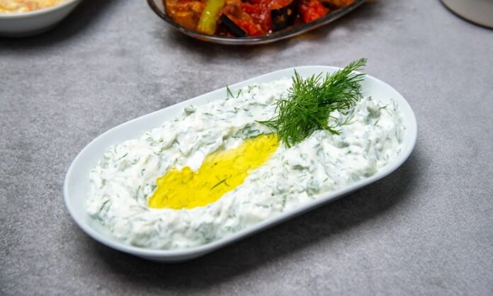 Haydari, özellikle kahvaltı sofralarının ve mezelerin vazgeçilmez tatlarından biridir. Yoğurt bazlı bu lezzetli meze, hem hafif hem de besleyici olmasıyla öne çıkar. Haydari, yüksek protein içeriği sayesinde kas ve kemik sağlığını desteklerken, probiyotik özelliği ile sindirim sistemine katkıda bulunur. İçerdiği sarımsak ve dereotu gibi doğal malzemeler, lezzetin yanı sıra sağlık açısından da avantaj sağlar. Konulu bir haber görseli.