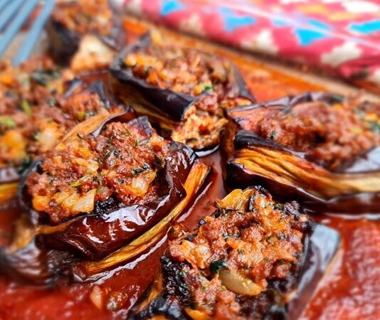 Türk mutfağının köklü ve sevilen yemeklerinden biri olan karnıyarık, patlıcanın en güzel hali olarak sofralarda yerini alıyor. İç harcında kullanılan kıyma, soğan, biber ve baharatların birleşimiyle ortaya çıkan bu yemek, hem doyurucu hem de lezzetli bir seçenek sunuyor. Özellikle yaz aylarında patlıcanın taze olduğu dönemlerde karnıyarık sofraların vazgeçilmezlerinden biri haline geliyor. Konulu bir haber görseli.