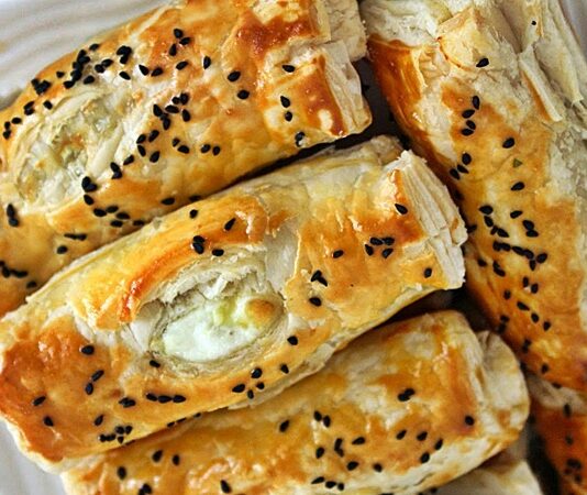 Peynirli börek, Türk mutfağının en özel ve geleneksel lezzetlerinden biridir. Çay saatlerinin en çok aranan eşlikçisi, misafir sofralarının baş tacı ve sabah kahvaltılarının olmazsa olmazı olan bu börek çeşidi, pratik hazırlanışıyla da gönülleri fetheder. Kat kat yufkaların arasına serilen lezzetli peynir harcı sayesinde ortaya çıkan doyurucu tat, hem günlük öğünlerde hem de özel davetlerde sıklıkla tercih edilir. Bugün, peynirli böreğin tarihinden yapılışına, farklı çeşitlerinden püf noktalarına kadar pek çok detayı keşfedeceğiz. Konulu bir haber görseli.