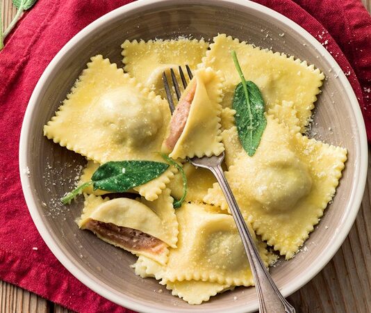 Ravioli, İtalyan mutfağının klasikleşmiş dolma makarna çeşitlerinden biridir. Genellikle küçük kare veya yarım ay şekillerinde hazırlanır ve iç harcı çeşitli malzemelerle doldurulur. Bu makarna türü, Orta Çağ’a kadar uzanan köklü bir geçmişe sahiptir ve İtalya’nın farklı bölgelerinde farklı içeriklerle hazırlanır. Konulu bir haber görseli.
