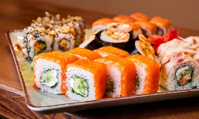 Sushi roll, Japon mutfağının en bilinen yemeklerinden biridir ve dünya genelinde ün kazanmıştır. İlk olarak Edo döneminde ortaya çıkan sushi, başlangıçta balığın pirinç içinde fermente edilmesiyle hazırlanıyordu. Zaman içinde bu yöntem değişti ve daha modern bir hale geldi. Özellikle 20. yüzyılın ortalarında Amerika’da popülerleşen sushi roll, farklı malzemelerin bir araya gelmesiyle çeşitlenerek bugünkü halini aldı. Konulu bir haber görseli.