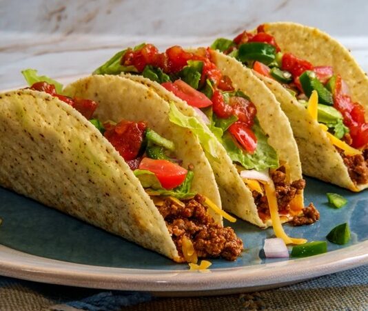 Taco, Meksika mutfağının en bilinen ve sevilen sokak lezzetlerinden biridir. Mısır veya buğday bazlı tortilla içine çeşitli malzemelerin doldurulmasıyla hazırlanır. Tarihi, yüzyıllar öncesine dayanan taco, Meksika halkının günlük beslenmesinde önemli bir yere sahiptir. Konulu bir haber görseli.