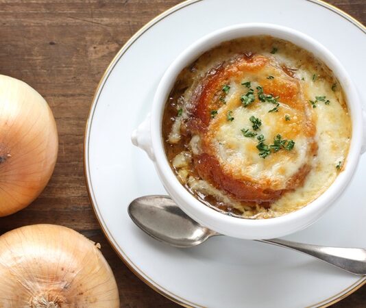 Dünya mutfağının en etkileyici ve simgesel lezzetlerinden biri olan Fransız soğan çorbası, hem Fransa’nın hem de küresel gastronomi dünyasının vazgeçilmezlerinden biri hâline gelmiştir. Orta Çağ’dan bu yana Fransız halk mutfağında kendine yer bulan bu çorba, zamanla uluslararası arenada da tanınmış ve birçok ülkenin restoran menülerinde yer almaya başlamıştır. Sade bir malzeme listesine sahip gibi görünen Fransız soğan çorbası, karamelize soğan, et suyu ve üzerine eklenen peynirli ekmek ile zenginleşerek hem doyurucu hem de aromatik bir deneyim sunar. Konulu bir haber görseli.