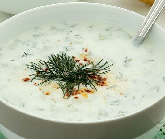 Cacık, Türk mutfağının en sevilen ve ferahlatıcı tariflerinden biri olarak öne çıkıyor. Özellikle yaz aylarında sofraları süsleyen bu yoğurt bazlı karışım, hem hafif hem de besleyici bir seçenek olarak dikkat çekiyor. Cacık hem öğle yemeklerinin yanında hem de akşam yemeklerinde meze olarak sunulabiliyor. Taze nane, salatalık ve sarımsak gibi malzemelerle hazırlanan cacık, sağlıklı ve lezzetli oluşuyla mutfakların vazgeçilmezi haline geliyor. Konulu bir haber görseli.