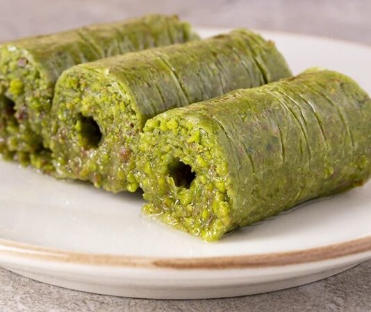 Gaziantep mutfağıyla özdeşleşen fıstık sarma, son yıllarda hem Türkiye’de hem de dünya genelinde gastronomi meraklılarının dikkatini çeken özel tatlılardan biri hâline geldi. İncecik açılan kadayıf hamurunun arasına bolca Antep fıstığı eklenerek hazırlanan bu eşsiz tatlı, hem görünümüyle hem de yoğun aromasıyla öne çıkıyor. Tatlı severlerin ilgisini çeken en önemli özelliklerinden biri ise tamamen doğal malzemelerle hazırlanmasına rağmen oldukça rafine bir lezzet sunması. Üstelik geleneksel tarifin modern dokunuşlarla birleşmesi, fıstık sarmayı son dönemde gurme restoranların da vazgeçilmezi yapıyor. Konulu bir haber görseli.