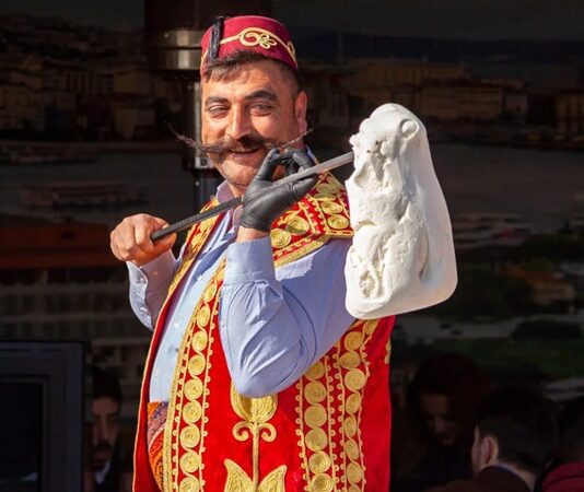 Türkiye’nin gastronomi mirası içinde kendine özgü yapısı, üretim tekniği ve kültürel arka planıyla öne çıkan Maraş dondurması, yalnızca bir tatlı değil aynı zamanda köklü bir geleneğin günümüze taşınmış hâli olarak kabul ediliyor. Özellikle yaz aylarında yoğun ilgi gören bu eşsiz lezzet, dayanıklı yapısı, bıçakla kesilebilen kıvamı ve kendine has aromasıyla klasik dondurmalardan ayrılıyor. Kahramanmaraş ile özdeşleşen bu ürün, bugün hem yerel ekonominin hem de Türkiye’nin tanıtım yüzlerinden biri hâline gelmiş durumda. Konulu bir haber görseli.