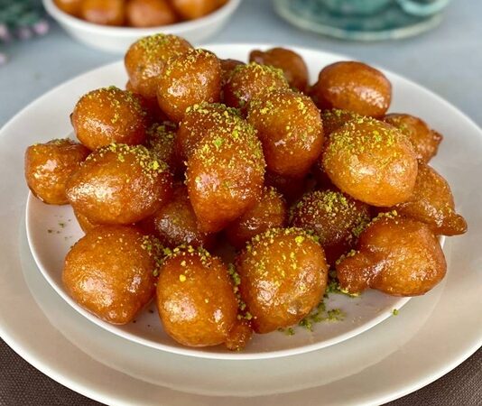 Türkiye’nin en sevilen tatlılarından biri olan lokma tatlısı, geçmişten bugüne gelen bir kültür mirasının lezzete dönüşmüş hâli olarak dikkat çekiyor. Osmanlı mutfağında önemli bir yere sahip olan lokma, günümüzde sokak lezzeti olarak yaygınlaşmış ve neredeyse her şehirde farklı hazırlanış şekilleriyle sunulmaya başlamıştır. Özellikle son yıllarda özel günlerde, hayır etkinliklerinde ve sosyal organizasyonlarda daha sık karşımıza çıkan lokma tatlısı, geleneksel tariften modern tariflere kadar geniş bir çeşitlilik sunmaya devam ediyor. Bu nedenle hem nostalji taşıyan hem de yeniliğe açık bir tatlı olarak gastronomideki yerini pekiştiriyor. Konulu bir haber görseli.