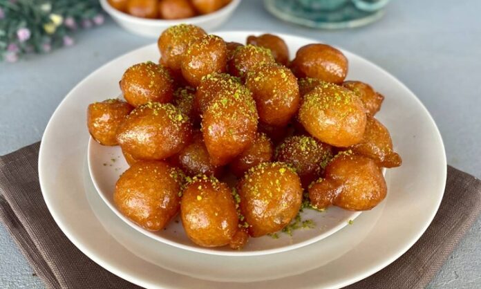 Türkiye’nin en sevilen tatlılarından biri olan lokma tatlısı, geçmişten bugüne gelen bir kültür mirasının lezzete dönüşmüş hâli olarak dikkat çekiyor. Osmanlı mutfağında önemli bir yere sahip olan lokma, günümüzde sokak lezzeti olarak yaygınlaşmış ve neredeyse her şehirde farklı hazırlanış şekilleriyle sunulmaya başlamıştır. Özellikle son yıllarda özel günlerde, hayır etkinliklerinde ve sosyal organizasyonlarda daha sık karşımıza çıkan lokma tatlısı, geleneksel tariften modern tariflere kadar geniş bir çeşitlilik sunmaya devam ediyor. Bu nedenle hem nostalji taşıyan hem de yeniliğe açık bir tatlı olarak gastronomideki yerini pekiştiriyor. Konulu bir haber görseli.