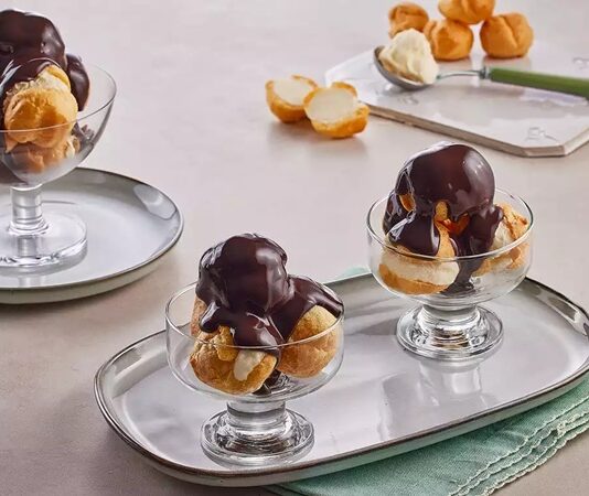 Fransız mutfağının en seçkin tatlılarından biri olan profiterol, uzun yıllardır hem restoranların hem de ev mutfaklarının en sevilen lezzetlerinden biri olarak yerini koruyor. Çıtır hamurun içindeki hafif krema ve üzerine dökülen yoğun çikolata sosuyla oldukça cezbedici bir tat sunan profiterol, özellikle misafir ağırlamalarında şık bir sunum oluşturmasıyla ön plana çıkıyor. Günümüzde pastane vitrinlerinde sıkça görülen bu tatlı, son dönemde ev yapımı tariflerin popülerleşmesiyle birlikte mutfakta daha da yaygın şekilde hazırlanıyor. Konulu bir haber görseli.