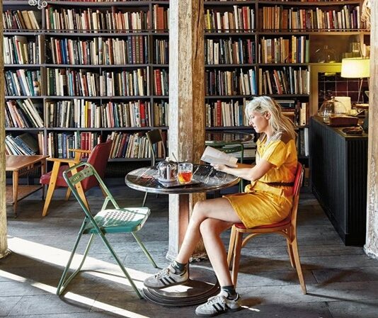 Kitap kafeler, modern şehir yaşamında okuma alışkanlığını sosyal deneyimle birleştiren özel mekânlar olarak öne çıkıyor. Sessizliği, kokusu ve atmosferiyle kitapçıları; sıcaklığı ve rahatlığıyla kafeleri buluşturan kitap kafeleri, özellikle gençler ve şehirli okur profili için önemli bir buluşma noktası hâline gelmiş durumda. Bu mekânlar, sadece kitap okunan yerler olmanın ötesinde, düşünmenin, üretmenin ve paylaşmanın merkezleri olarak dikkat çekiyor. Konulu bir haber görseli.