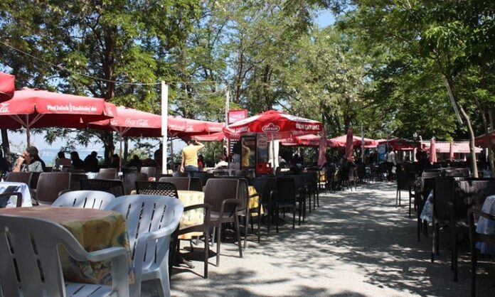 Çay bahçeleri, Türkiye’de gündelik yaşamın en köklü ve en yaygın sosyalleşme alanlarından biri olarak öne çıkıyor. Park kenarlarında, sahil şeritlerinde, mahalle aralarında ya da tarihi meydanlarda karşımıza çıkan çay bahçeleri, her yaştan insanın bir araya geldiği ortak buluşma noktaları olarak dikkat çekiyor. Bu mekânlar, sadece çay içilen yerler değil; sohbetin, dinlenmenin ve gündelik hayatın paylaşıldığı açık hava alanları olarak şehir kültürünün ayrılmaz bir parçası hâline gelmiş durumda. Konulu bir haber görseli.